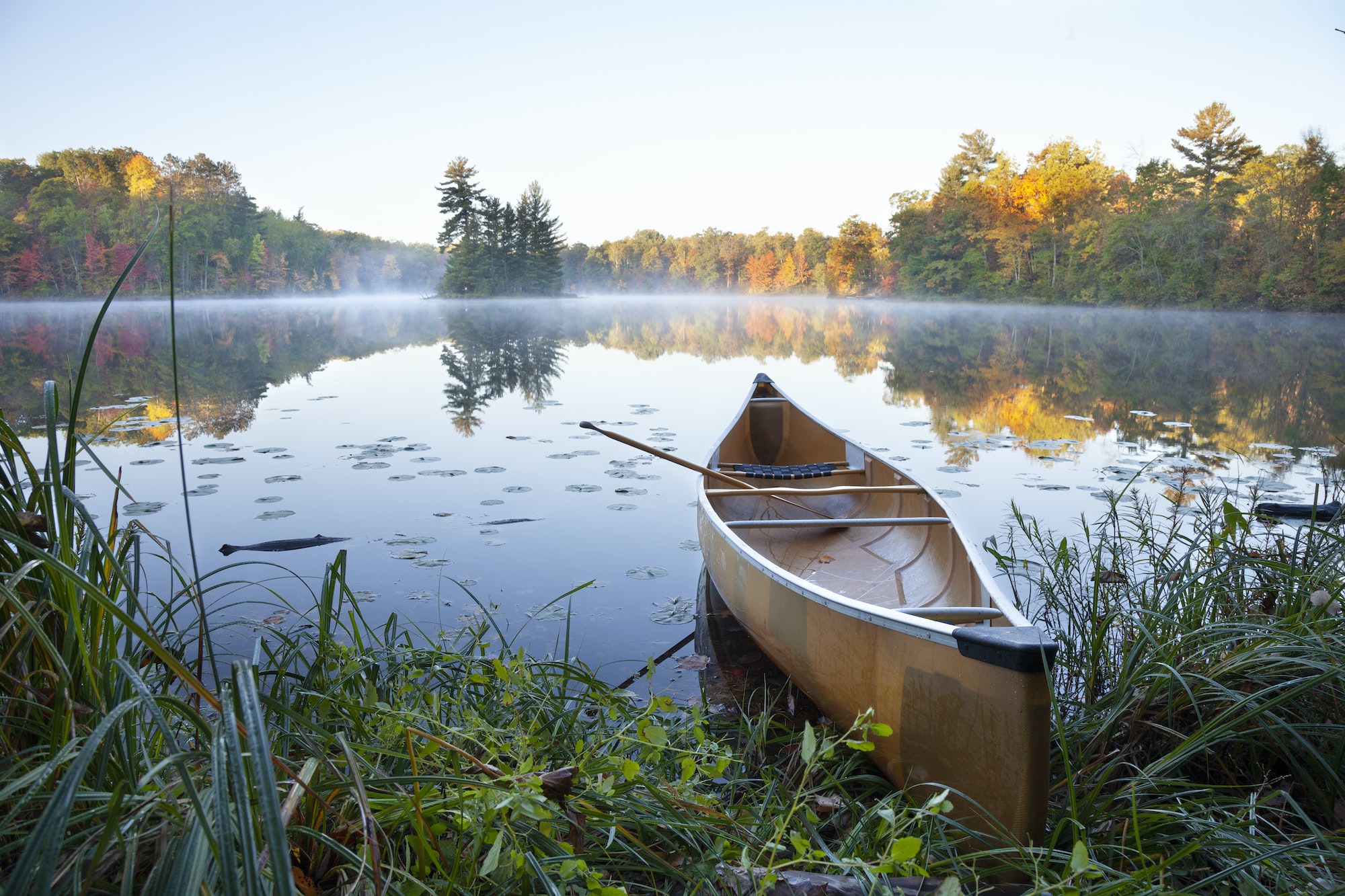 Yellow canoe on shore of calm lake with island at sunrise during autumn